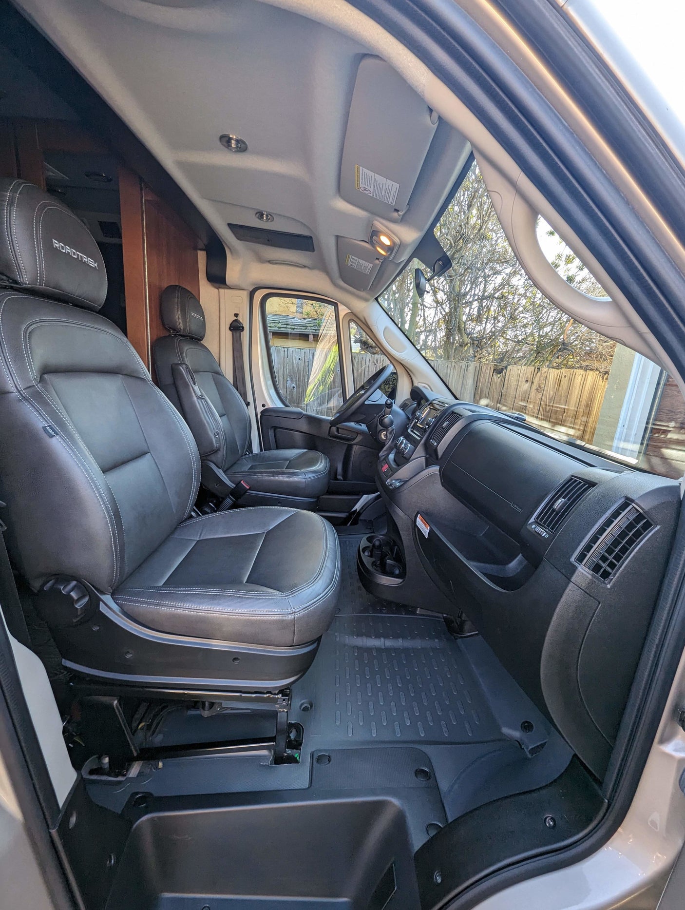 Clean front cabin of a Roadtrek RV rental, featuring black leather seats, dashboard, and durable floor mats.