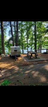 An RV rental camper trailer is set up at a serene lakeside campsite with a picnic table, perfect for nature getaways.