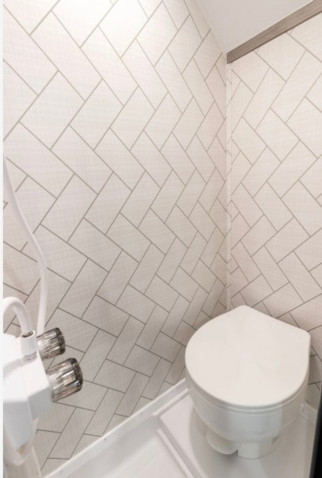 Clean RV rental bathroom featuring a compact toilet and stylish subway tile pattern walls.