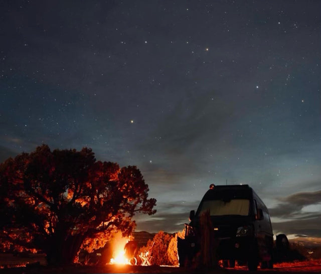  surrounded by trees under a cloudy sky.|An RV rental parked under a starry night sky