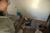 RV rental kitchen: A person cooks a meal on a portable gas stove, with a "Happy Camper" mug beside them.