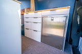 Organized RV rental interior: modern white drawers, integrated stainless steel fridge, and warm LED countertop lighting.