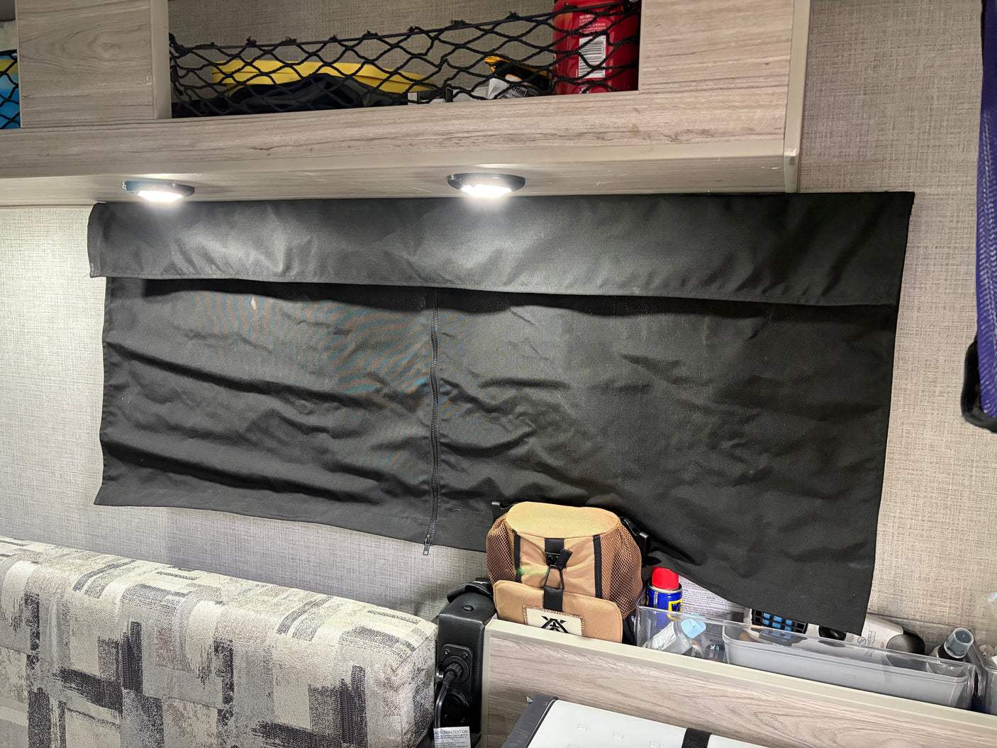 RV rental interior: Black blackout window shade, overhead netted storage, bright LED lights, and patterned seating.