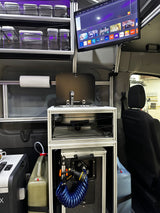 Inside an RV rental: a smart TV, compact kitchen with Dometic sink, fridge, shower, and organized storage containers.