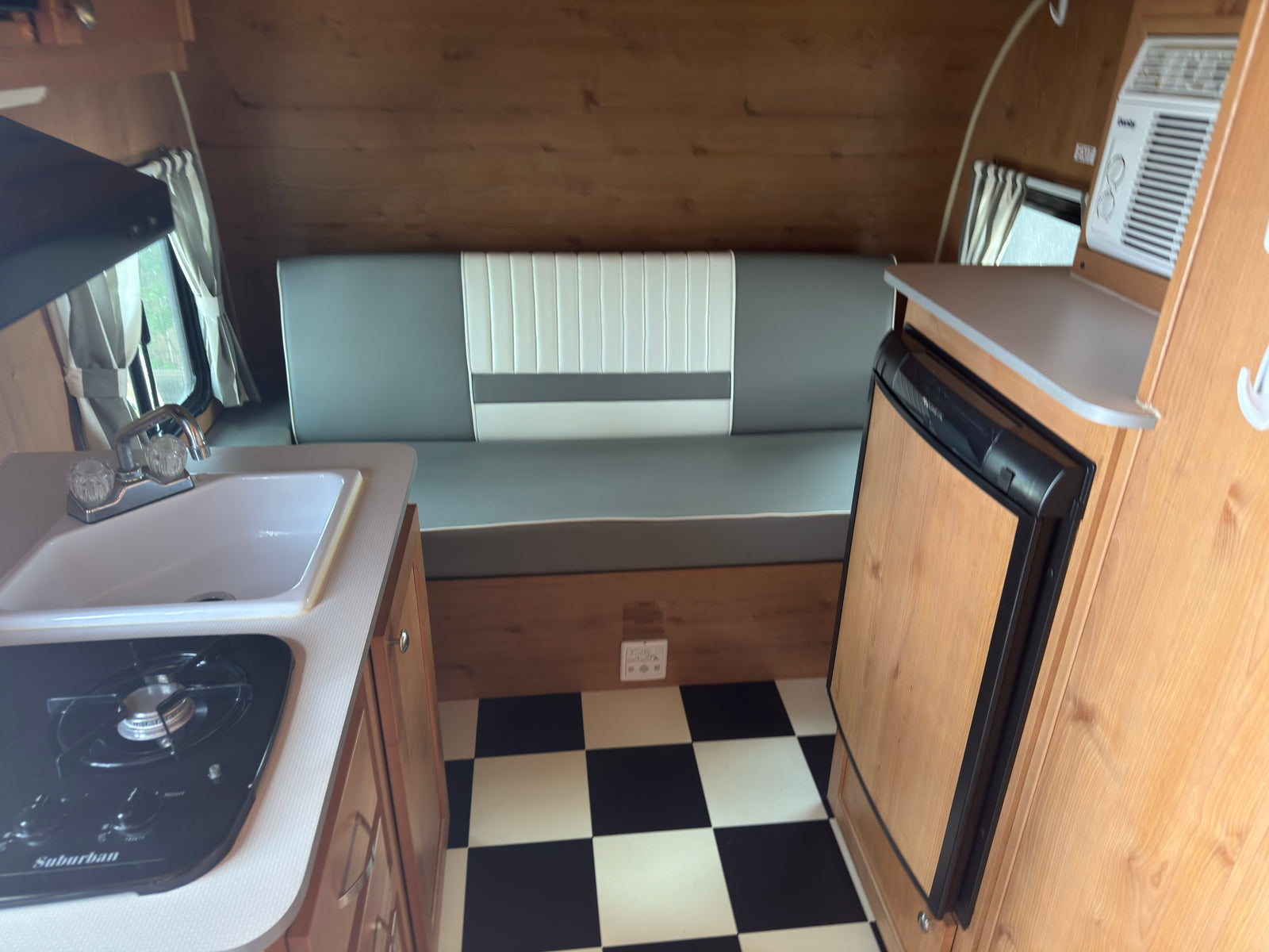 Retro RV rental interior features a compact kitchen with stove and sink, dinette seating, fridge, AC, and classic black-and-white checkered floor.
