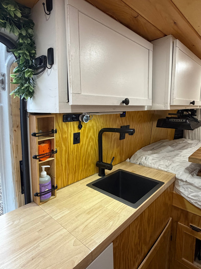 Cozy RV rental interior: compact kitchen with a black sink, wooden counter, white cabinets, & bed. — photo 6