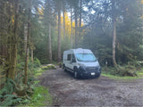 A white rv rental campervan is parked at a serene forest campsite #9, surrounded by towering, moss-draped trees.