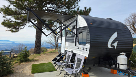 Scenic rv rental campsite with a travel trailer, chairs, and an extended awning overlooking a panoramic mountain and valley view.