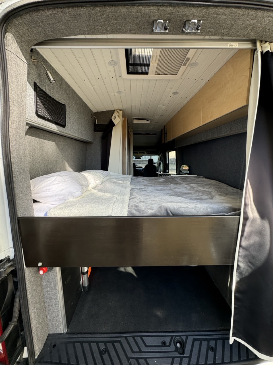 Spacious camper van interior, perfect for rv rental adventures. Features a raised bed, storage, and cozy amenities.