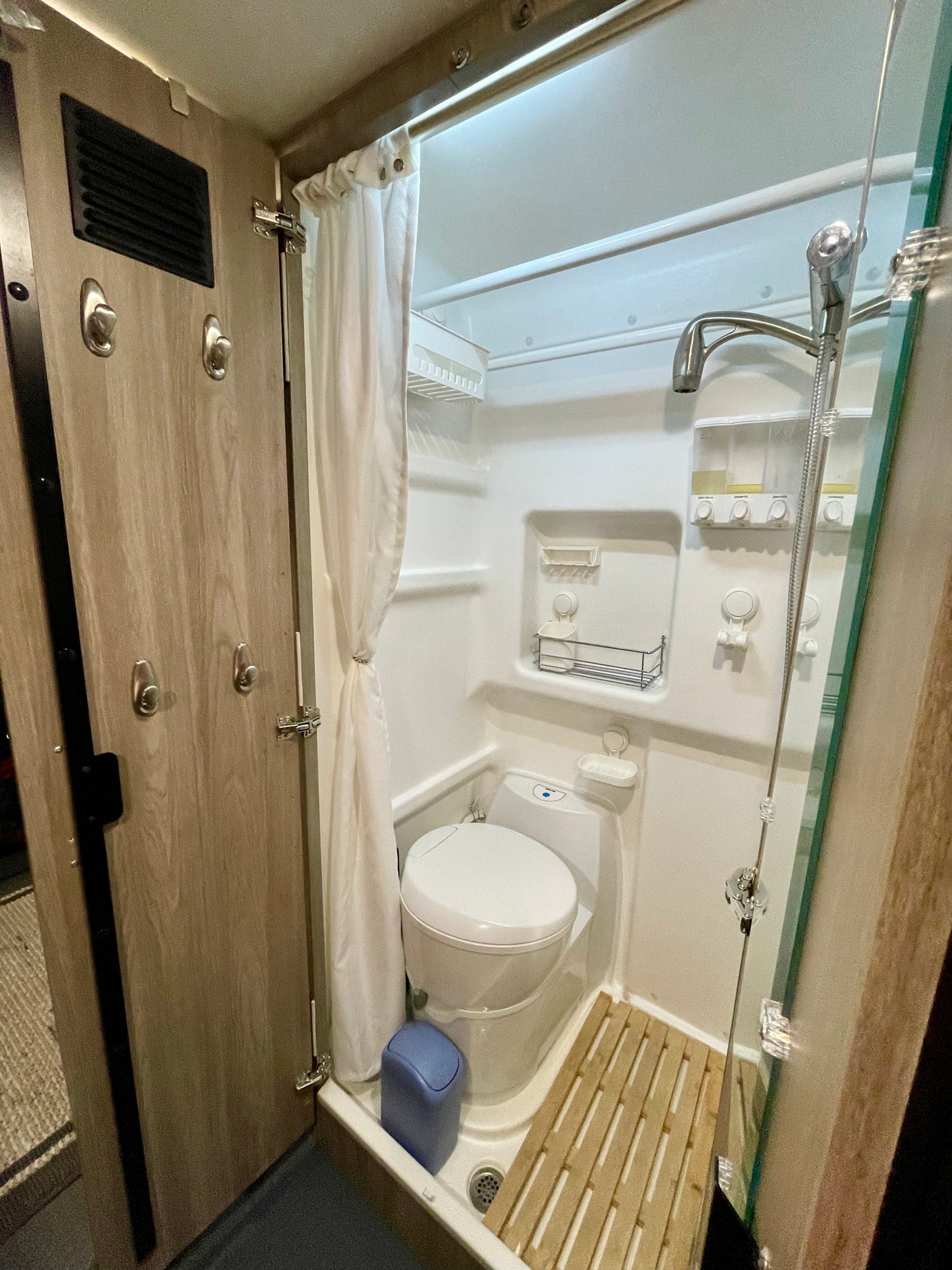 Inside an RV rental: a compact wet bath with a toilet, shower, and curtain. Hooks and shelves provide storage.