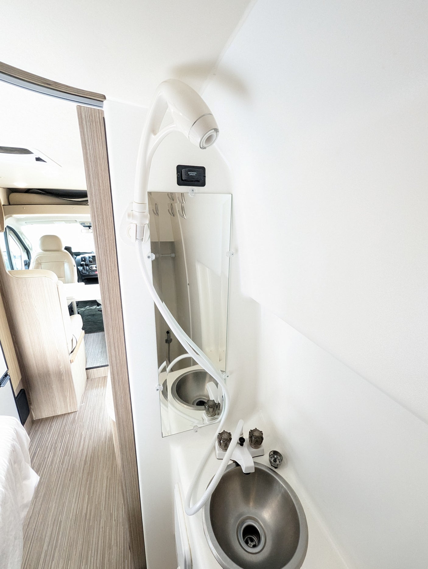 RV rental interior: compact bathroom with sink, shower, and mirror, offering a view of the main cabin.