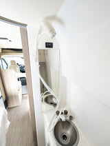 RV rental interior: compact bathroom with sink, shower, and mirror, offering a view of the main cabin.