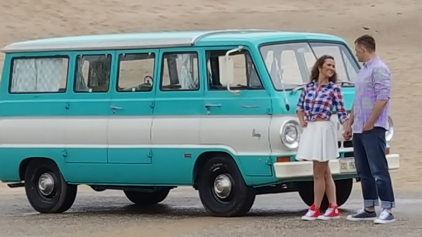 Smiling couple stands by their classic turquoise and white RV rental, ready for adventure.