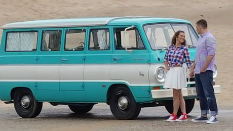 Smiling couple stands by their classic turquoise and white RV rental, ready for adventure.