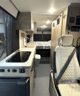 Clean rv rental interior: kitchen with sink/stovetop, cozy rear bed, and passenger seat, ready for adventure.