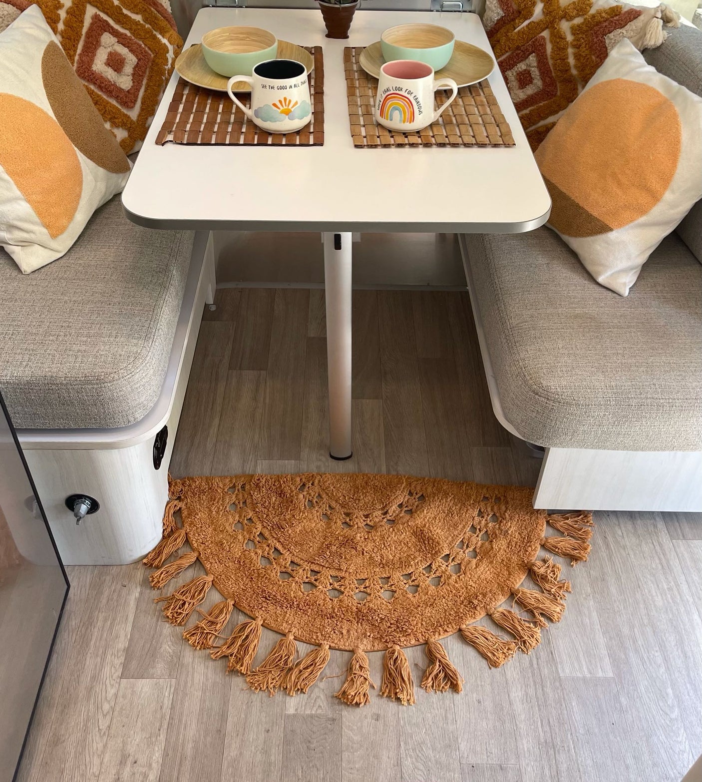 Cozy RV rental interior with a dining area. Features a table, bench seats, decorative pillows, and a cheerful rug.