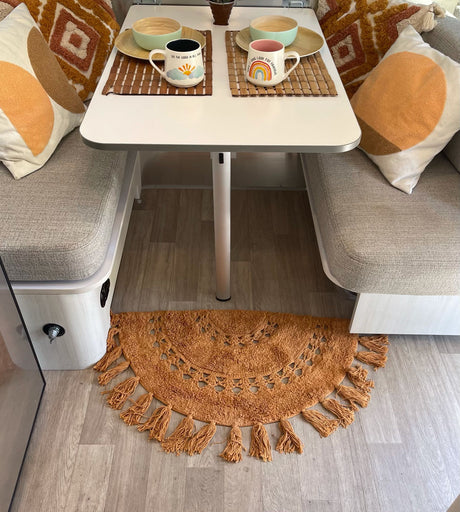 Cozy RV rental interior with a dining area. Features a table, bench seats, decorative pillows, and a cheerful rug.