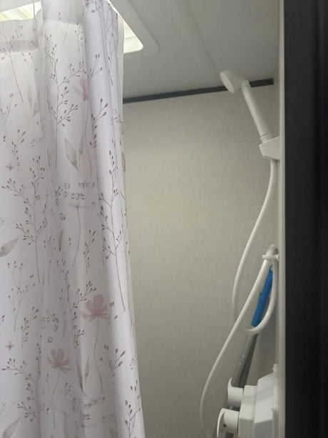 RV rental shower: Light floral curtain, white showerhead with hose, and a blue scrubber, ideal for a compact RV bathroom.