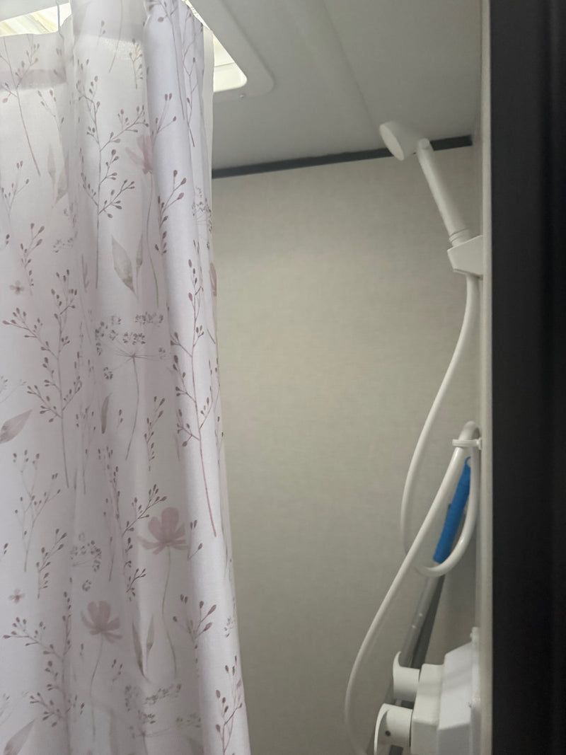 RV rental shower: Light floral curtain, white showerhead with hose, and a blue scrubber, ideal for a compact RV bathroom. — photo 7