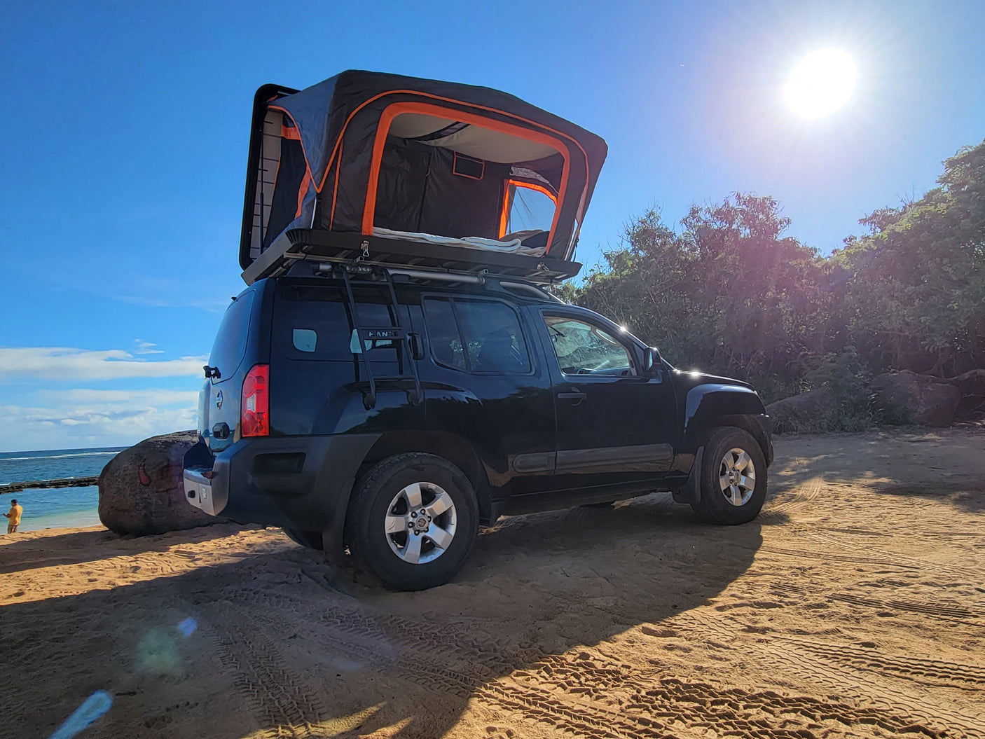 Explore off-grid with this black SUV featuring a rooftop tent, perfect for a unique rv rental experience on a sunny beach.