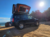 Explore off-grid with this black SUV featuring a rooftop tent, perfect for a unique rv rental experience on a sunny beach.