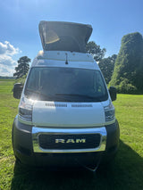 Front view of a white Ram ProMaster pop-top camper van for rv rental, parked on sunny green grass.