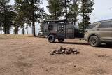 A gray teardrop camper trailer towed by an SUV at a rustic campsite with a fire pit, perfect for an rv rental outdoor adventure.
