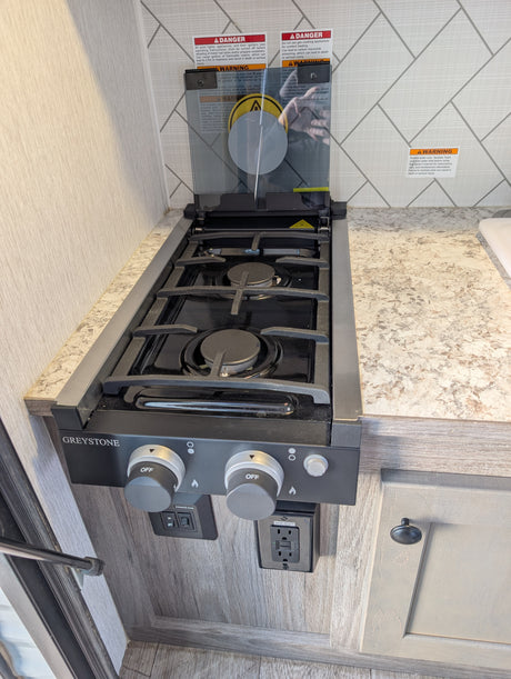 This RV rental kitchen features a Greystone gas stovetop with a glass cover, burner controls, and safety warnings for use.