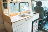 Compact camper van kitchen with sink, induction cooktop, fridge, and control panel. Perfect for an rv rental adventure!