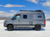 Gray Winnebago Revel 4x4 camper van for rv rental on vast white salt flats, mountains under blue sky.