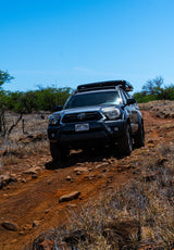 Rugged Toyota Tacoma truck with a rooftop tent tackles a rocky Hawaiian trail. An ideal adventure vehicle, more versatile than a typical RV rental.