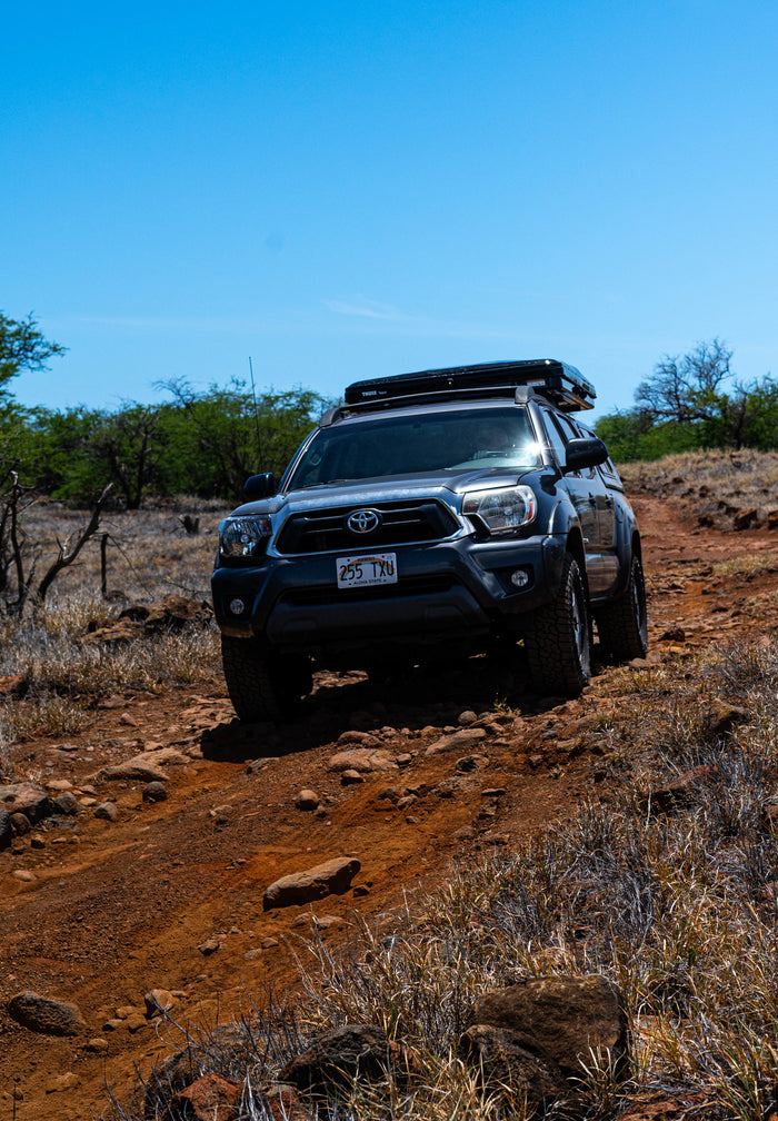 Rugged Toyota Tacoma truck with a rooftop tent tackles a rocky Hawaiian trail. An ideal adventure vehicle, more versatile than a typical RV rental.