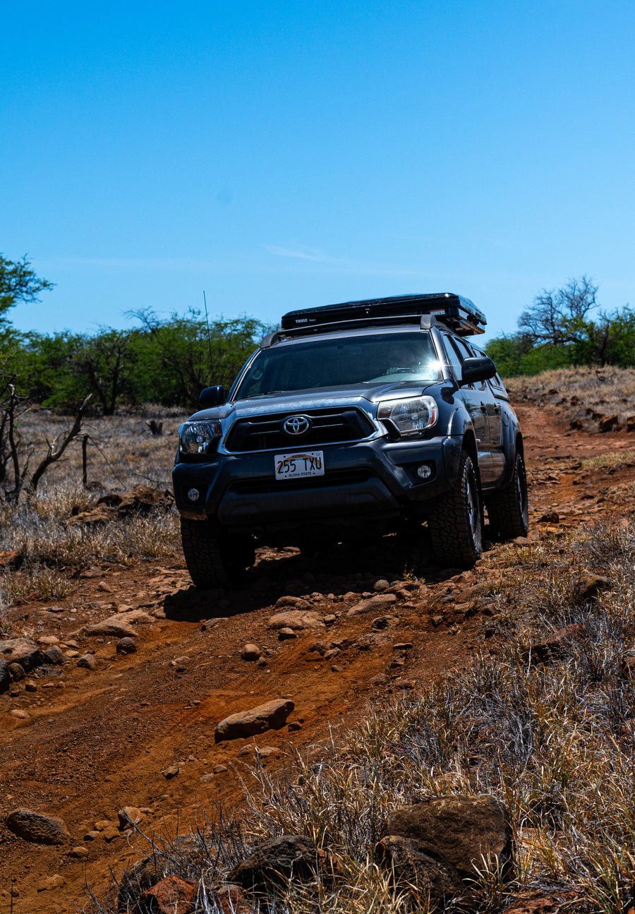 Rugged Toyota Tacoma truck with a rooftop tent tackles a rocky Hawaiian trail. An ideal adventure vehicle, more versatile than a typical RV rental.