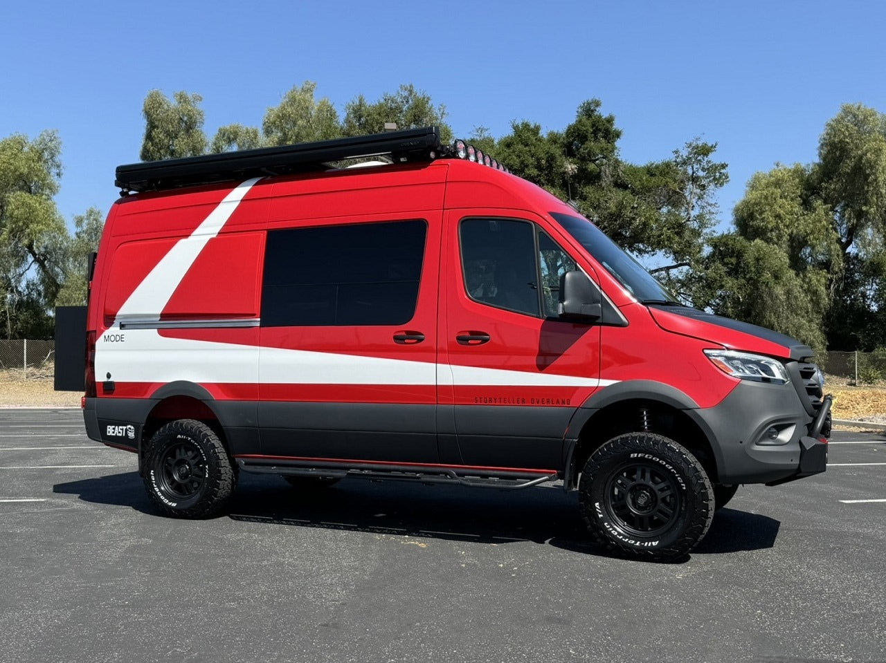 A bold red and white Storyteller Overland adventure van, ready for your next RV rental. Features include off-road tires and roof lights.