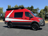A bold red and white Storyteller Overland adventure van, ready for your next RV rental. Features include off-road tires and roof lights.