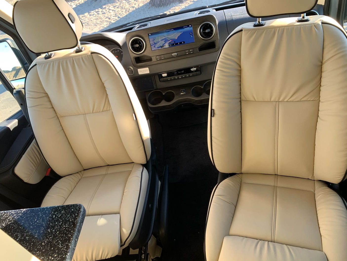Explore comfort in this RV rental! View the front cabin with plush seats, navigation, and dashboard from a traveler's perspective.