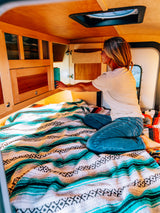 Woman finds a book in her cozy RV rental, sitting on a colorful patterned blanket. Perfect for mobile living.