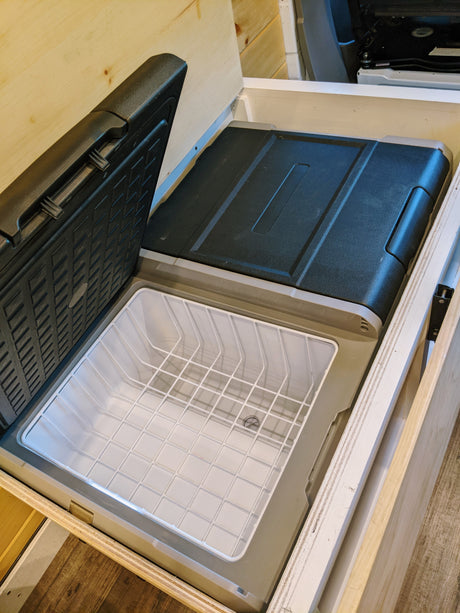 RV rental: Portable refrigerator/freezer with open lid and wire basket, built into custom wooden storage.
