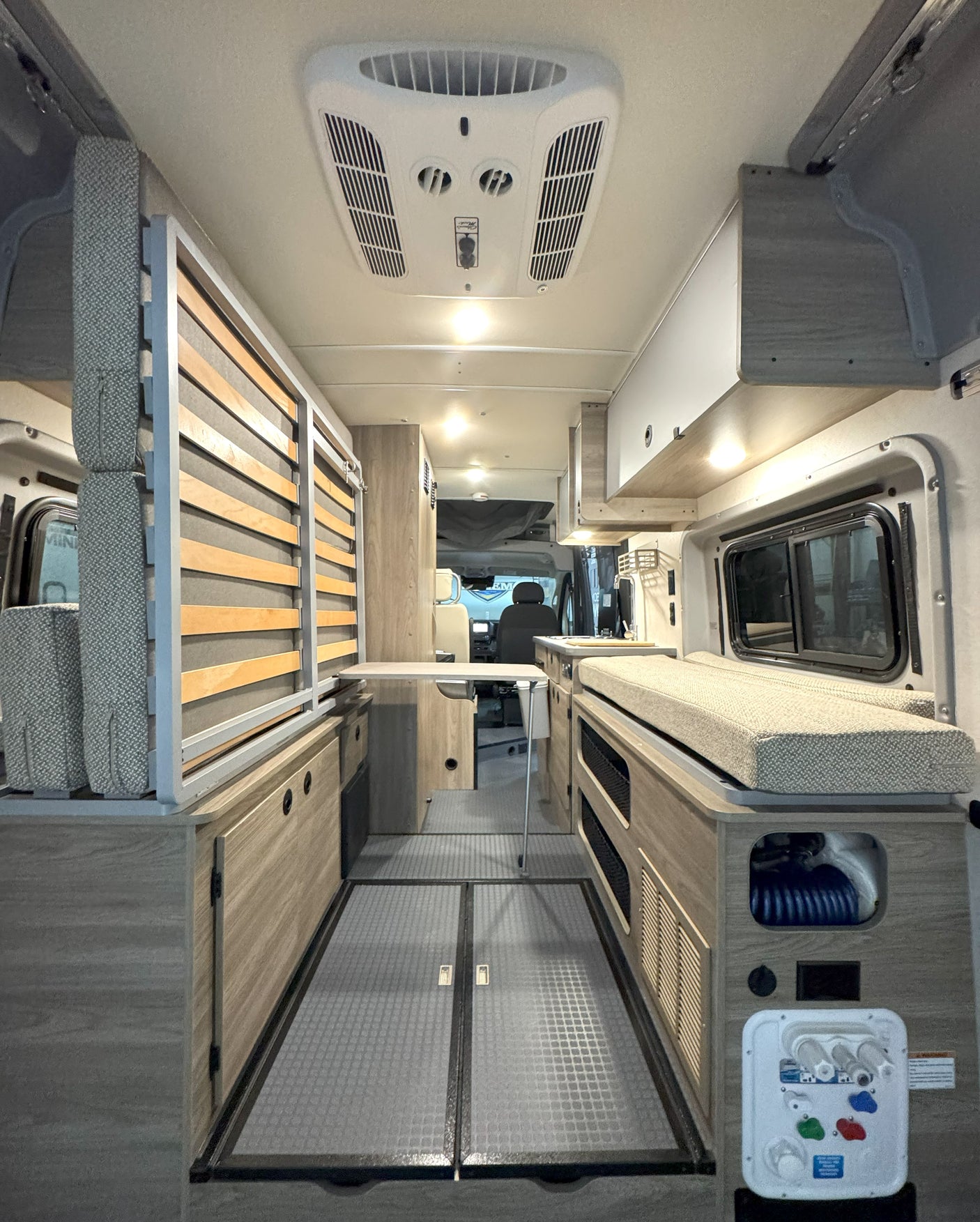This rv rental interior features a convertible slatted bed, comfy bench seating, a fold-down table, and a water utility panel.