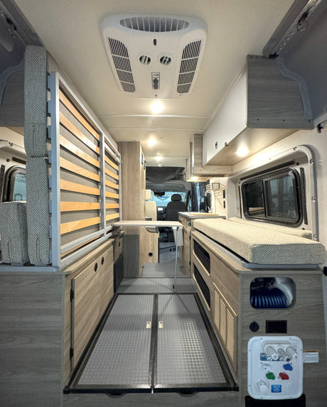 This rv rental interior features a convertible slatted bed, comfy bench seating, a fold-down table, and a water utility panel.