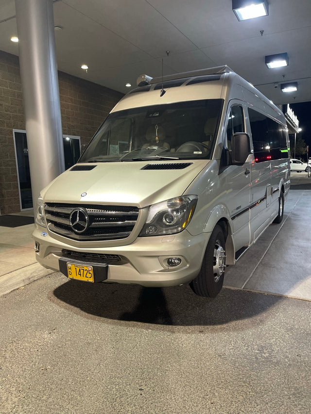 A champagne-colored Mercedes-Benz Sprinter RV rental (campervan) is parked at night, brightly lit from above.
