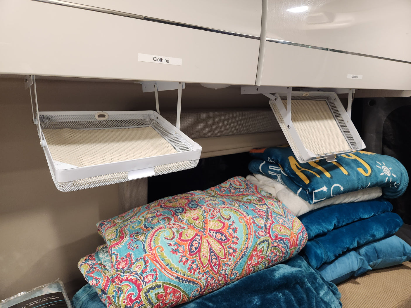 RV rental overhead storage: labeled "Clothing" mesh baskets hang above neatly folded blankets and quilts.