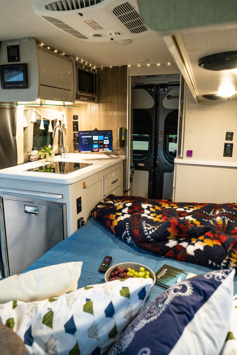 Explore a comfortable RV rental interior: kitchen, cozy bed with blanket, TV for entertainment, and overhead amenities. — photo 11