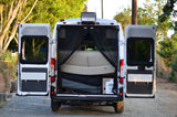 Rear view of an RV rental camper van with open doors, revealing light interior seating, mesh screens, and storage. Ideal for travel.