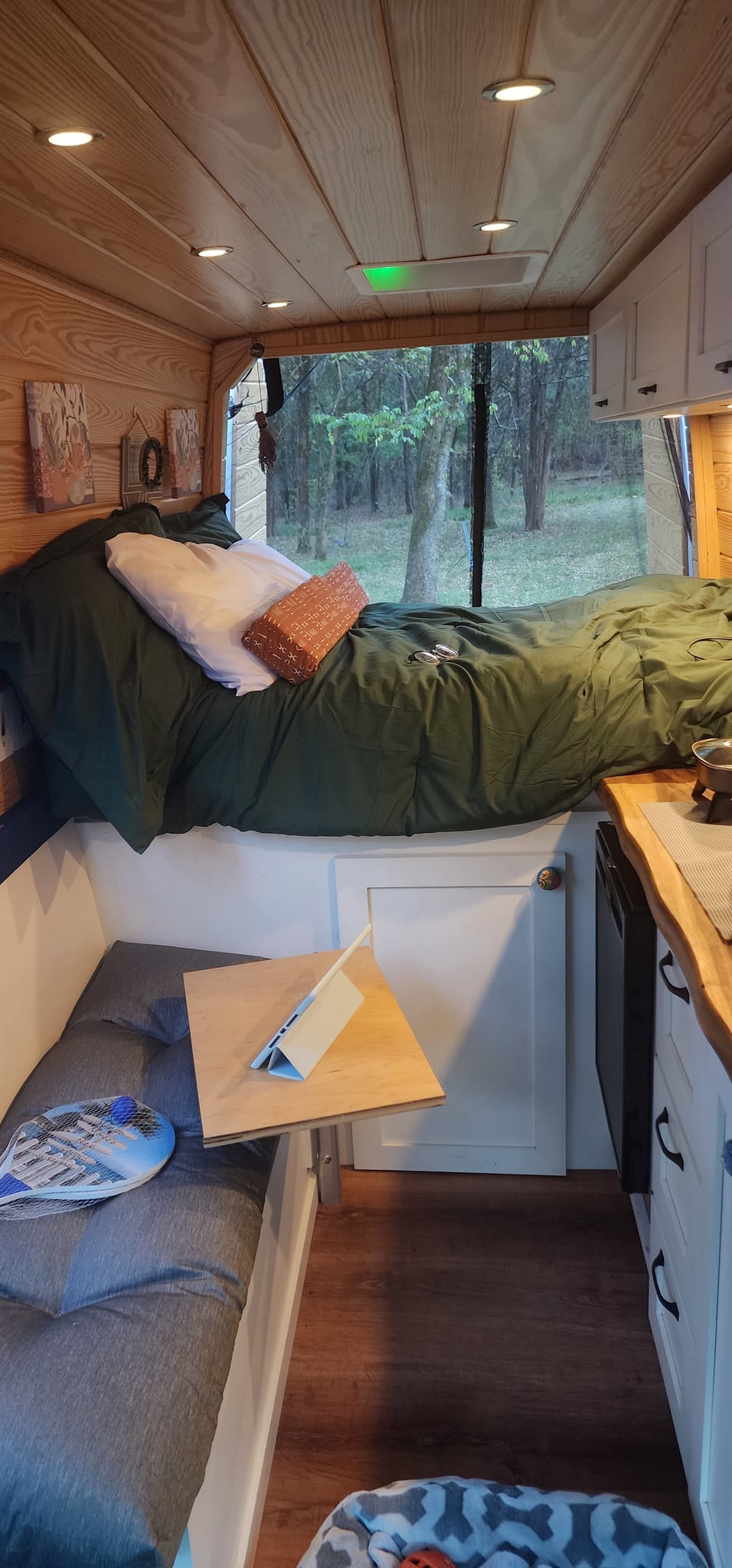 This RV rental interior features a cozy bed with forest views
