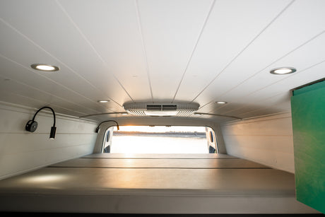 Inside this RV rental: a cozy bed, planked ceiling with bright lights, AC unit, and reading lamps. Ready for your next adventure!