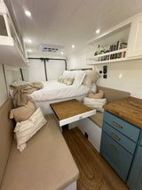 This bright and cozy RV rental interior features a comfortable bed, pull-out dining table, and compact kitchen.