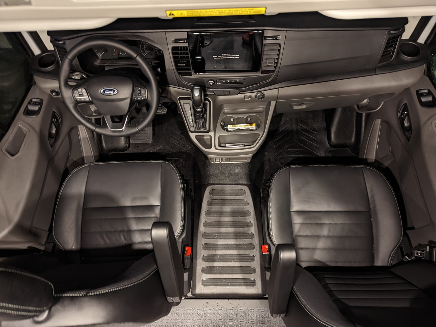 Overhead view of a modern Ford van interior, ideal for rv rental. Features dashboard, steering wheel, shifter, and two black leather seats.