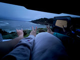Cozy RV rental view: hands make peace, rock-on, and shaka signs overlooking an overcast ocean and cliffs.