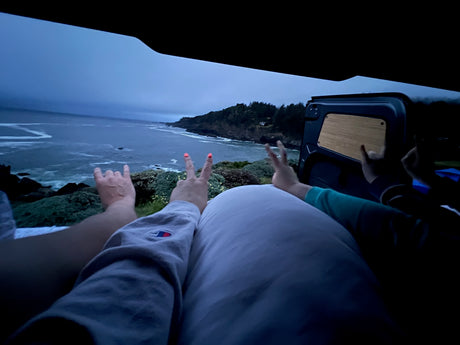 Cozy RV rental view: hands make peace, rock-on, and shaka signs overlooking an overcast ocean and cliffs.
